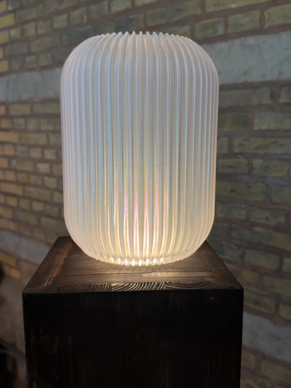 The Noorian Freestanding light in Clear, lit from its foot on a dark plinth
